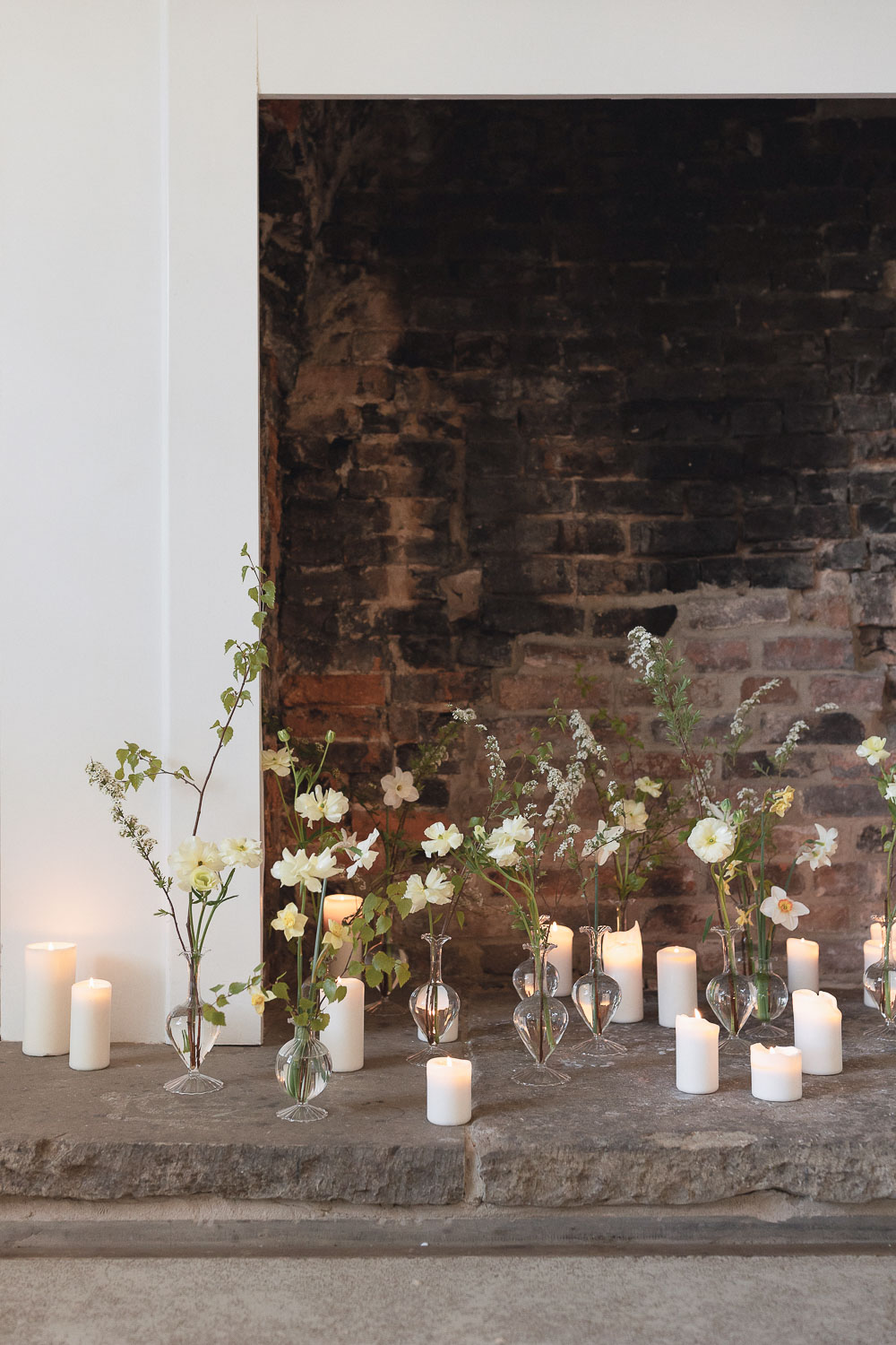 Bud vase arrangements positioned in fireplace hearth with candles. Photo ©Daisy Price Photography