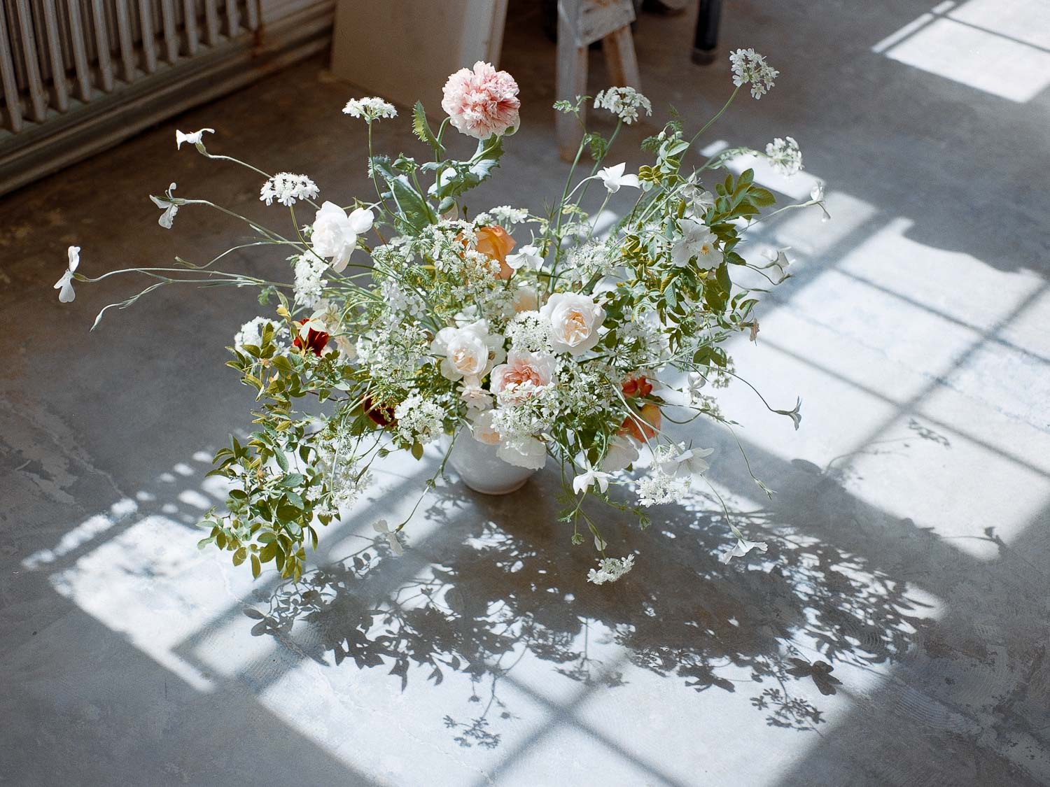 Large natural arrangement made in antique vessel positioned on the floor casting dramatic shadow